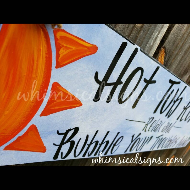 May include: Wooden sign with a painted orange sun and orange triangle accents on a light blue background. The sign reads "Hot Tub Kinda Life" and "Bubble Your Troubles Away" in black script. The website "whimsicalsigns.com" is also visible.