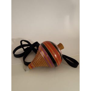 May include: A traditional wooden spinning top with a black cord. The top is decorated with orange, black, and purple stripes. It features a wooden peg and a metal tip, a classic toy.