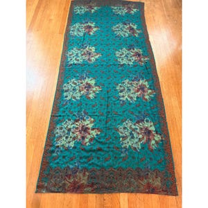 May include: A white ceramic mug with a black handle and the text "But First, Coffee" in a bold, black font. The mug is set against a blurred background, suggesting a cozy setting.