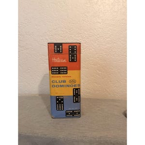 May include: A vintage "Halsam Club Dominoes" box. The box is rectangular with a color block design in red, yellow, and blue. The box features the text "double twelve" and "91 pieces". The dominoes are visible on the box.