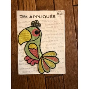 Puede incluir: Un parche de costura Talon appliqués con un diseño de loro colorido. El loro tiene un pico amarillo, cuerpo verde y detalles en rojo y rosa. El parche está sobre un fondo blanco con texto.