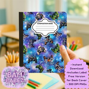 May include: Composition book with a vibrant galaxy-themed cover featuring video game controllers and mummy-themed controllers. The cover has a white label that says "COMPOSITION BOOK". The notebook is held by a hand.