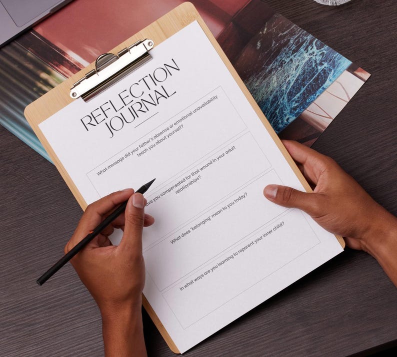 May include: A wooden clipboard with a silver clip holding a white sheet of paper with the words "REFLECTION JOURNAL" printed at the top. The paper has lined sections with questions. A black pen is held over the paper.