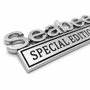 Pu&ograve; includere: Un'emblema cromato con la parola "Seabee" in lettere in rilievo sopra una placca rettangolare. La placca riporta le parole "SPECIAL EDITION" in lettere nere.