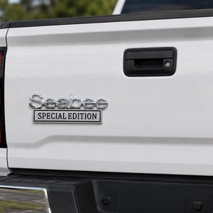 Pu&ograve; includere: Primo piano del retro di un camion bianco con maniglia nera e fanale posteriore rosso. L'emblema cromato recita "Seabee SPECIAL EDITION". Il cassone &egrave; pulito, con un paraurti nero.