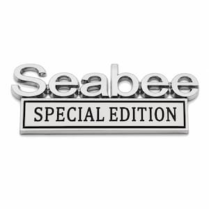 Pu&ograve; includere: Un'emblema cromato "Seabee" con il testo "SPECIAL EDITION" su una placca rettangolare. L'emblema ha una superficie riflettente ed &egrave; posto su uno sfondo bianco.
