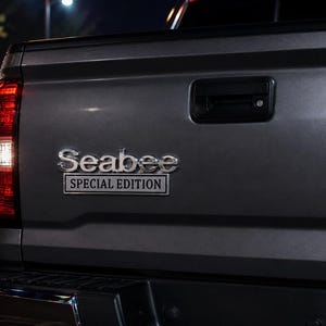 Pu&ograve; includere: Primo piano del portellone posteriore grigio di un pick-up. L'emblema cromato recita "Seabee Special Edition". Il fanale posteriore &egrave; rosso con una luce di retromarcia bianca. Lo sfondo &egrave; scuro, suggerendo la notte.