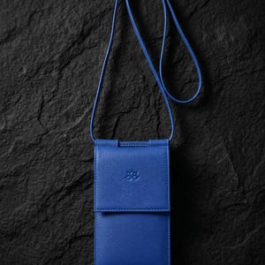 May include: A vibrant blue vertical crossbody phone bag with a textured finish, a fold-over flap closure, and a long matching shoulder strap. The front of the bag features a small, embossed floral logo centred on the flap, with clean stitching.