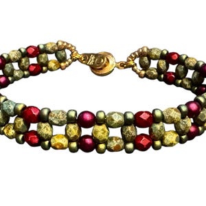 May include: A beaded bracelet with a gold clasp. The bracelet features three rows of beads in shades of red, gold, and olive green. The beads are a mix of round and faceted shapes. The clasp is gold-toned.