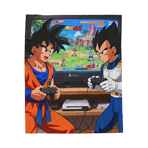 May include: A blanket featuring a vibrant illustration of two anime characters playing a video game. One character wears an orange gi, the other a blue and white outfit. The TV screen displays a colorful game scene.