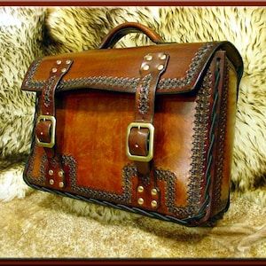 Könnte beinhalten: Eine braune Ledertasche mit aufwendigen Nähten und Messing-Akzenten. Die Tasche hat zwei Schnallen und einen oberen Griff.