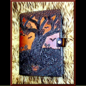 Peut inclure: Un journal en cuir marron avec un motif ciselé d'un arbre avec des oiseaux et des écureuils. Le journal a une fermeture à rabat avec un bouton en métal.