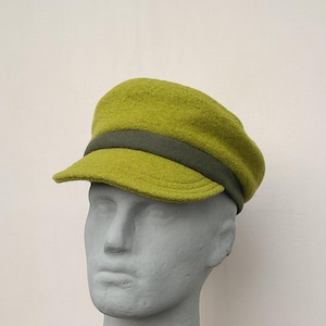 May include: A chartreuse-colored, wool newsboy cap with a dark olive green band. The cap has a short brim and a rounded crown. The hat is displayed on a gray mannequin head against a white background. A stylish accessory.