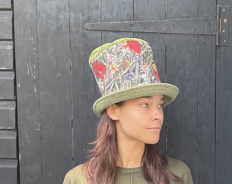Könnte beinhalten: Ein grüner Zylinderhut mit floralem Muster, darunter rote Mohnblumen und andere Blumen. Der Hut hat eine grüne Krempe und ein grünes Samtfutter. Ein ausgefallenes Modeaccessoire.