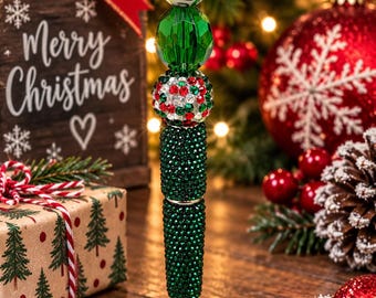 May include: A decorative pen featuring a stack of beads in various textures and colours, including dark green rhinestones, a white bead with a colourful string light pattern, a faceted green bead, and a red, green, and white rhinestone bead.