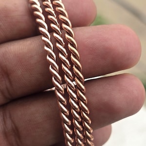 May include: Three copper-colored, twisted metal bangles. The bangles have a rope-like design, with each strand of metal tightly wound together. The bangles are displayed against a blurred background.