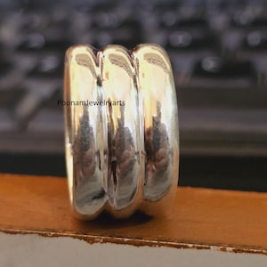 May include: A polished silver ring featuring three distinct, rounded, parallel bands joined together into a single piece. The surface of the metal is highly reflective and smooth. The text PoonamJewelryarts is visible on the ring.
