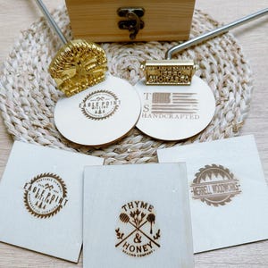 May include: A collection of wood-burning tools and branded wooden coasters. The coasters feature various logos and text, including "Eagle Point" and "Handcrafted." A wooden box and a woven mat are also visible.