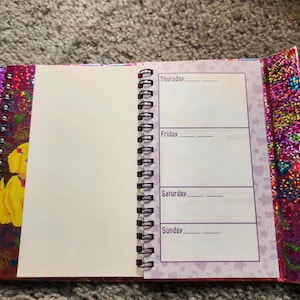 Puede incluir: Diario de espiral abierto con una p&aacute;gina en blanco y un horario semanal de jueves a domingo. La portada y los bordes del diario tienen un acabado brillante e iridiscente con un dise&ntilde;o floral. Las p&aacute;ginas son blancas con texto morado.