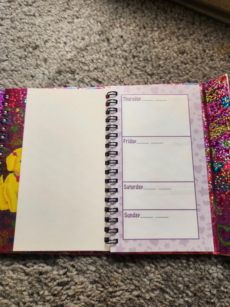 Puede incluir: Diario de espiral abierto con una p&aacute;gina en blanco y un horario semanal de jueves a domingo. La portada y los bordes del diario tienen un acabado brillante e iridiscente con un dise&ntilde;o floral. Las p&aacute;ginas son blancas con texto morado.