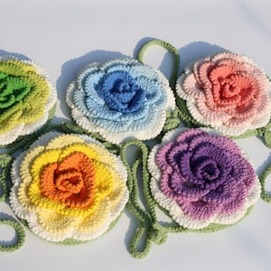 Könnte beinhalten: Fünf farbenfrohe gehäkelte Blumentaschen. Jede Tasche hat eine andere Farbe, darunter Grün, Blau, Rosa, Gelb und Lila. Die Taschen haben einen weißen Rand und grüne Träger. Die Taschen haben einen Durchmesser von etwa 20 cm.