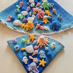 May include: Two blue crocheted blankets with a white scalloped edge, adorned with various crocheted sea creatures. The creatures include octopuses, starfish, fish, and shells in a variety of colors, such as pink, yellow, and blue.