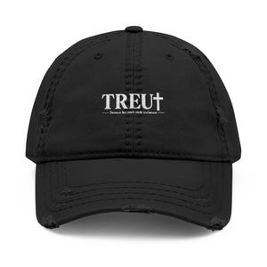 Könnte beinhalten: Eine schwarze, distressed Baseballkappe mit weißer Stickerei, die das Wort TREU zeigt, wobei ein Kreuz das U ersetzt, sowie den darunter liegenden Text Denn er hat mich nicht verlassen.