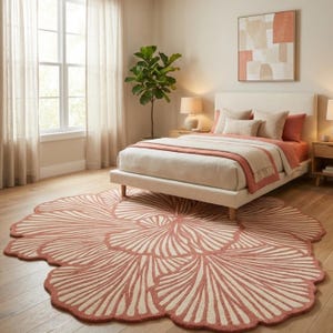 May include: A bedroom with a large, floral-shaped rug in dusty rose and cream. The rug is the focal point, complementing the neutral-toned bed linens and decor. A bed with a cream-coloured headboard and wooden legs is in the background.