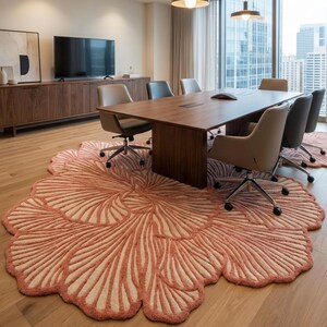 May include: A coral and cream floral rug dominates a conference room. The rug's design is a large, stylized flower. The room also features a wooden table, chairs, and a cityscape visible through a large window.
