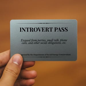May include: A gray Introvert Pass card held by a hand. The card features the text "INTROVERT PASS" and states the holder is excused from social obligations. The card is approved by the Department of Social Energy Conservation.