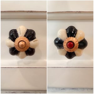 May include: Decorative cabinet knobs with a floral design. The knobs feature a black and cream petal pattern with a gold center. One knob has a red center. These knobs are a stylish addition to any furniture piece.