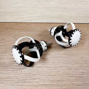 May include: Two black and white metal cabinet knobs with a decorative, twisted design. The knobs have a white finish with black accents.