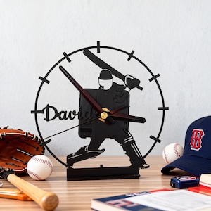 May include: A black cricket-themed clock with the name "David" on the clock face. The clock features a silhouette of a cricket player in action. Baseball glove, baseball, and a baseball cap are also visible.