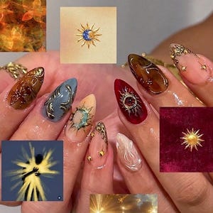 May include: A set of almond-shaped artificial nails featuring a variety of designs including deep red, brown, and blue tones with gold sun and moon metallic accents, intricate swirling patterns, and small gold beads applied to the nail surfaces.