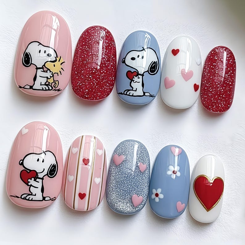 May include: A set of ten oval-shaped artificial nails with various designs. The designs include Snoopy holding a heart, red glitter, pink hearts, and white and pink stripes. The nails are in shades of pink, red, blue, and white.