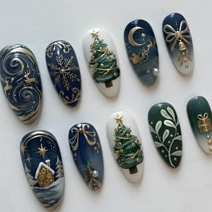 May include: A collection of ten artificial nails with various winter and holiday-themed designs. The nails feature detailed artwork including snowflakes, Christmas trees, reindeer, and a sleigh, all in a palette of navy, gold, white, and green.