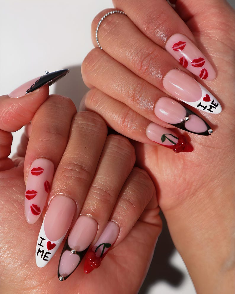 May include: Long, almond-shaped acrylic nails with a pink base and white tips. Designs include red lips, cherries, and the text "I ❤️ ME". Some nails have black accents and rhinestones.