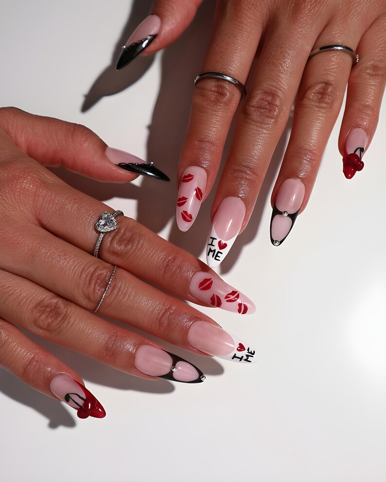 May include: A set of long, almond-shaped acrylic nails. Some nails feature a French tip design with red lip prints, while others have black tips with a jewel accent. The phrase "I ❤️ ME" is written on two nails.