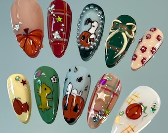 May include: A set of ten almond-shaped, decorated artificial nails. Designs include pumpkins, Snoopy, plaid patterns, and floral accents. Colors include orange, red, green, and beige, with embellishments of pearls and rhinestones.