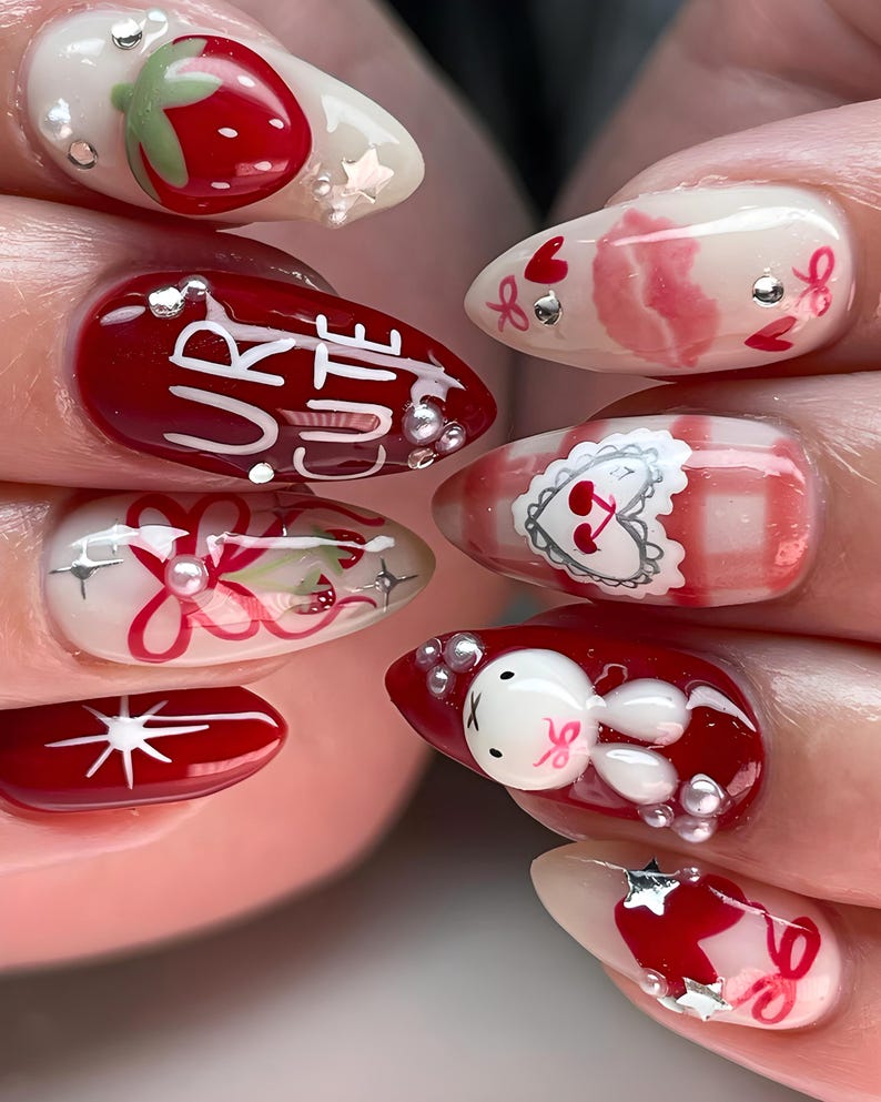 May include: A set of almond-shaped, decorated fingernails. Designs include strawberries, bows, hearts, and a bunny. One nail features the words "UR CUTE". Embellishments include silver stars and small pearls. The nails are painted in shades of red, white, and pink.