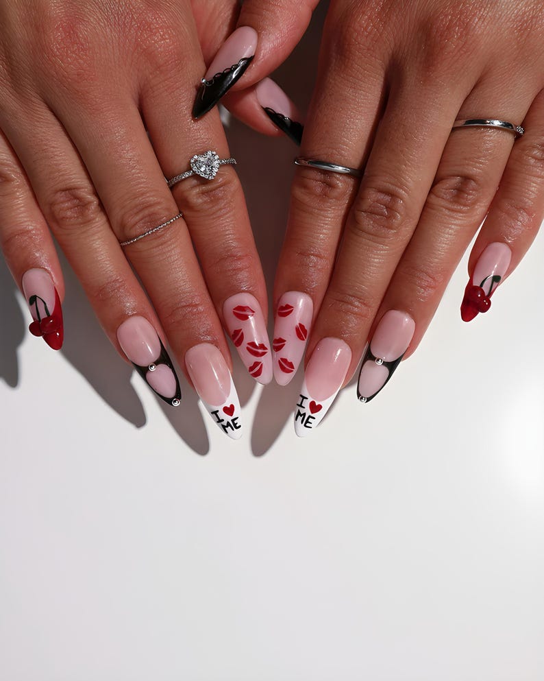May include: A close-up of manicured nails with various designs. Some nails feature a cherry design, others have red lips, and some have the text "I ❤️ ME". The nails are long and almond-shaped, with a pink and white color scheme.
