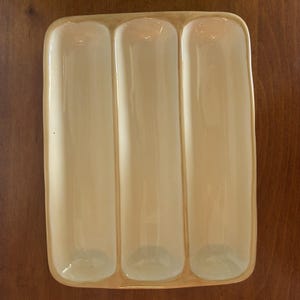 May include: A rectangular ceramic serving tray with a glossy cream-colored finish, featuring three distinct, elongated, vertical recessed compartments separated by raised dividers, with rounded corners and smooth edges.