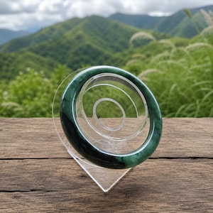 May include: A smooth, circular jade bangle bracelet featuring a polished surface with deep forest green and translucent emerald green color variations, displayed upright on a clear acrylic stand to showcase its solid, continuous ring form.