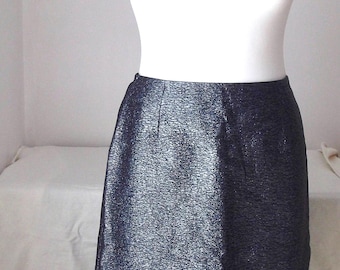 May include: A dark blue pencil skirt with a textured, shimmering fabric. The skirt is displayed on a white mannequin, showcasing its straight silhouette and knee-length hem. The skirt's fabric has a subtle sheen.