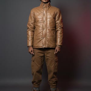K&ouml;nnte beinhalten: Hellbraune Lederjacke mit Knopfleiste und hohem Kragen, kombiniert mit passender Cargohose und braunen Stiefeln. Das Outfit ist ein komplettes Set, perfekt f&uuml;r einen robusten, Outdoor-Look. Die Jacke hat ein gestepptes Design.