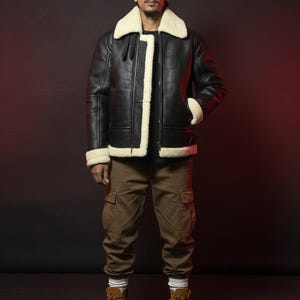 May include: A black leather jacket with a cream-colored shearling collar and trim. The jacket has a zipper closure and two front pockets. The person is wearing brown cargo pants and tan work boots.
