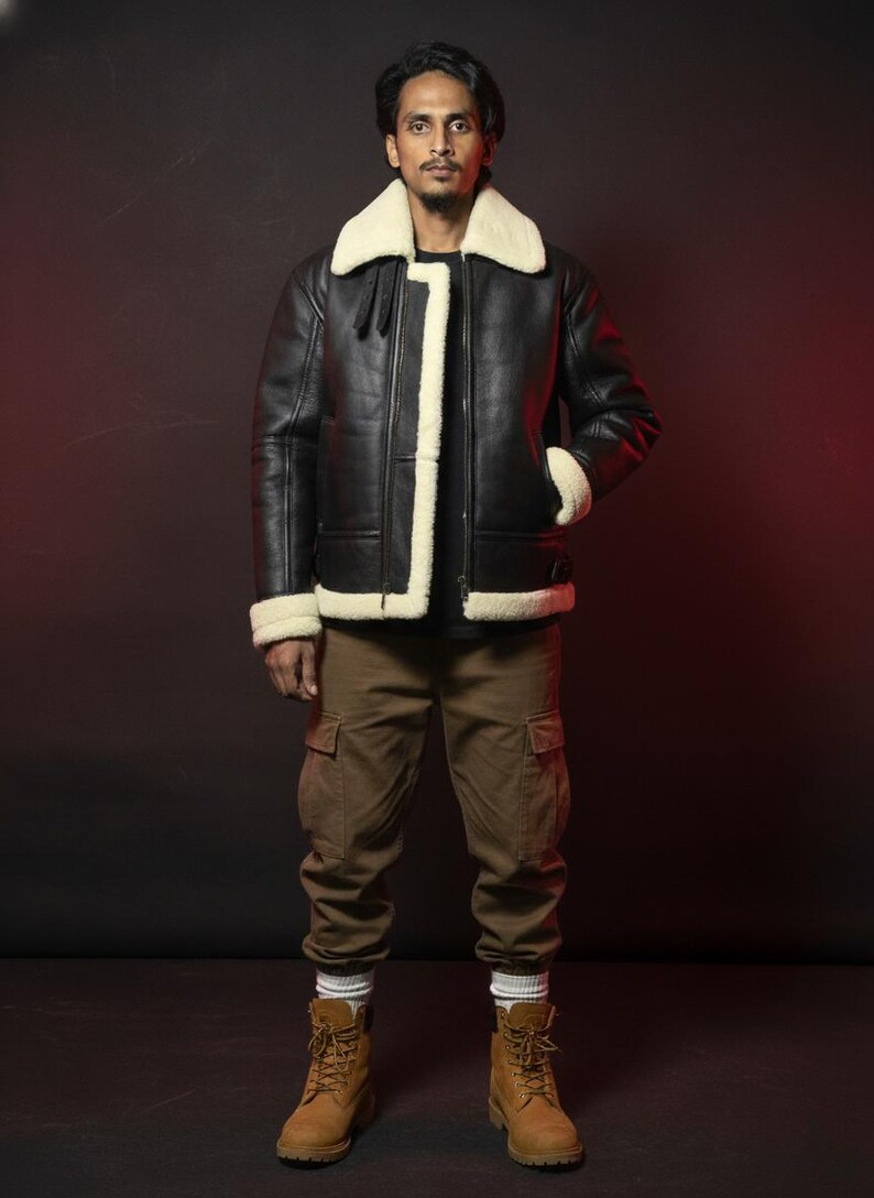 May include: A black leather jacket with a cream-colored shearling collar and trim. The jacket has a zipper closure and two front pockets. The person is wearing brown cargo pants and tan work boots.