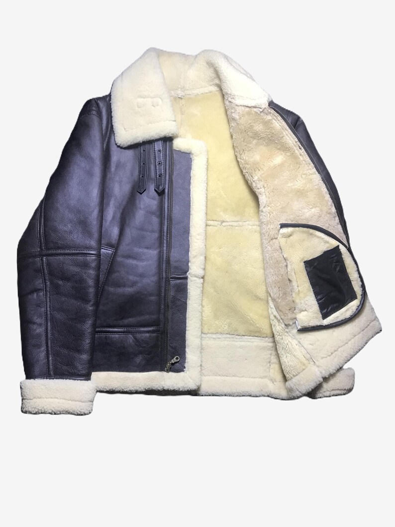 May include: A dark blue leather jacket with a cream-colored shearling lining and collar. The jacket features a zip-up front, two front pockets, and a classic aviator style. The cuffs and hem are trimmed with cream-colored shearling.