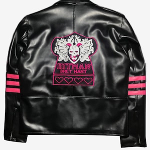 May include: Black leather jacket with pink accents. Features a pink and white embroidered design on the back with the text "HITMAN BRET HART". Includes pink stripes on the sleeves and four pink heart outlines.