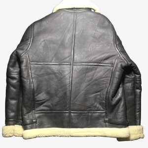 May include: A black leather jacket with a cream-colored shearling collar and trim. The jacket has a classic design with visible stitching and paneling. The back view showcases the jacket's structure and details.